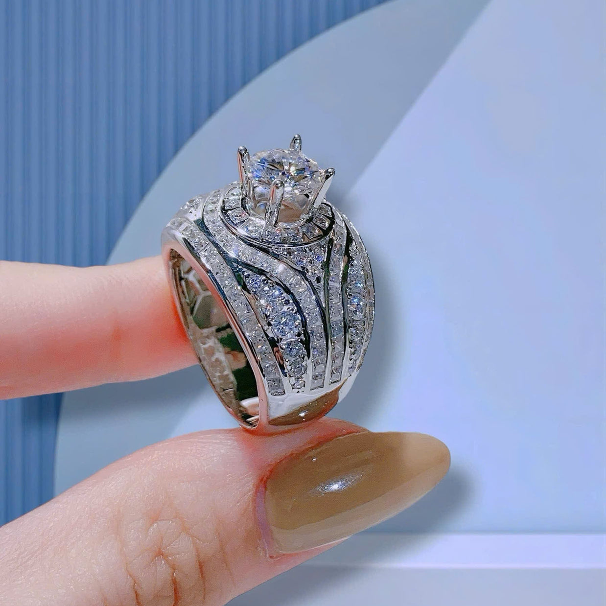 Silver ring with intricate design held by a hand against a light blue background