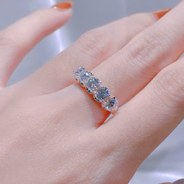 Silver ring with multiple gemstones on a person's finger against a neutral background
