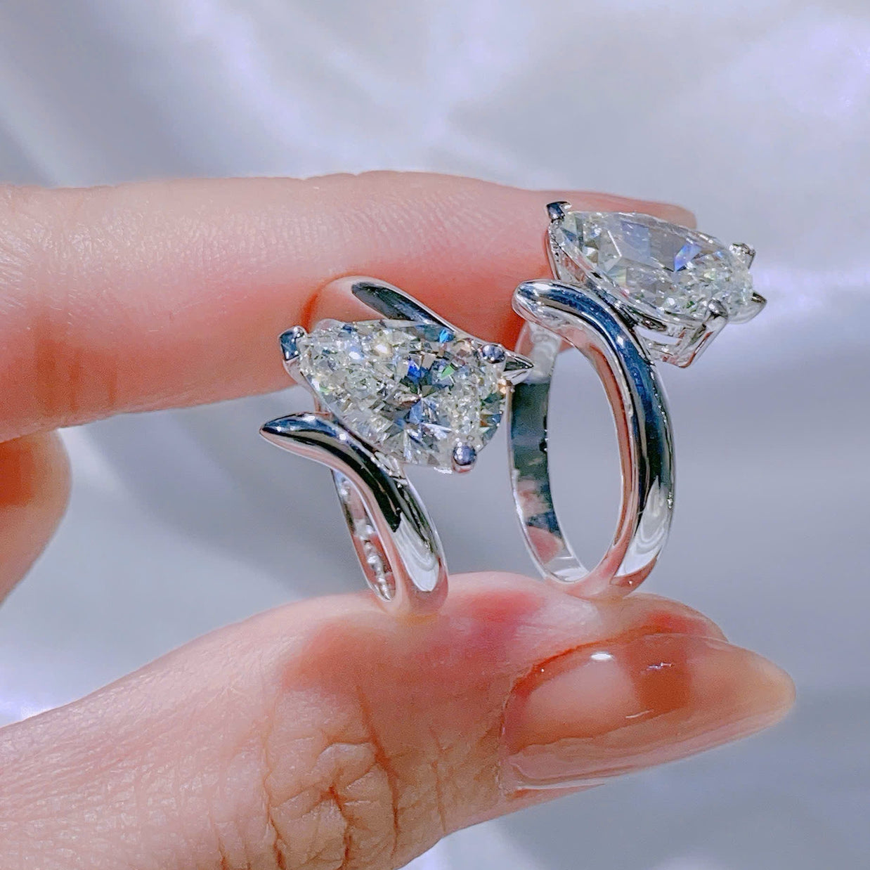 Silver ring with two large gemstones held between fingers against a neutral background