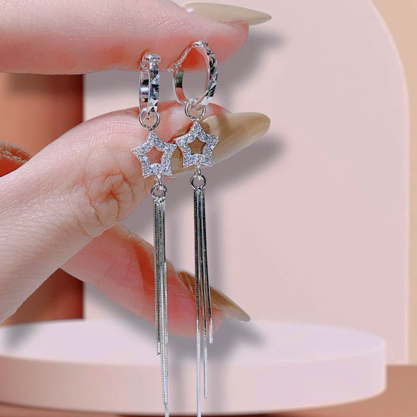 Silver star-shaped earrings held by a hand against a neutral background