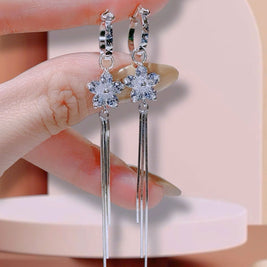 Silver star-shaped earrings with tassels held by a hand against a neutral background