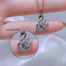 Silver swan-shaped necklace with gemstones held between fingers on a light background