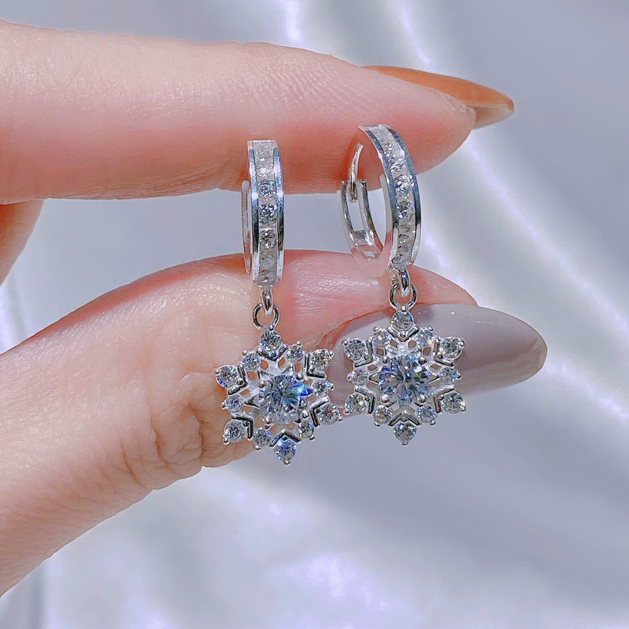 Snowflake-shaped earrings held between fingers against a neutral background