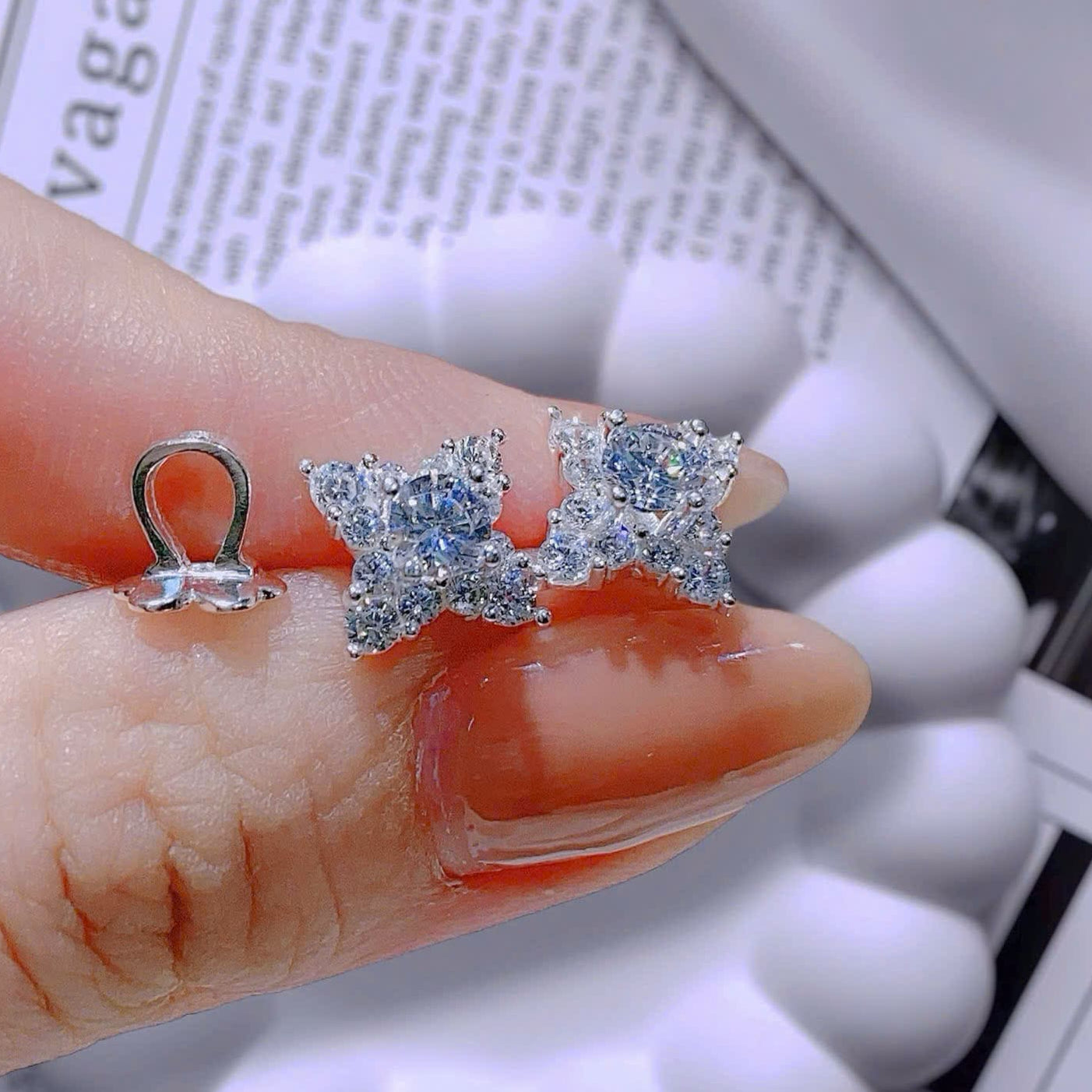 Star-shaped earrings held between fingers with a blurred newspaper background