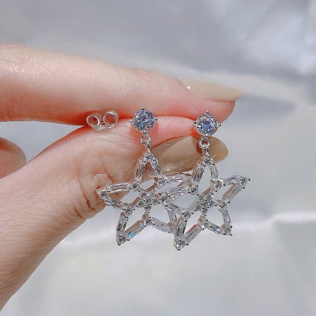 Star-shaped earrings held by a hand with a blurred background