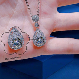 Teardrop-shaped diamond necklace and earrings on a hand with a blue background