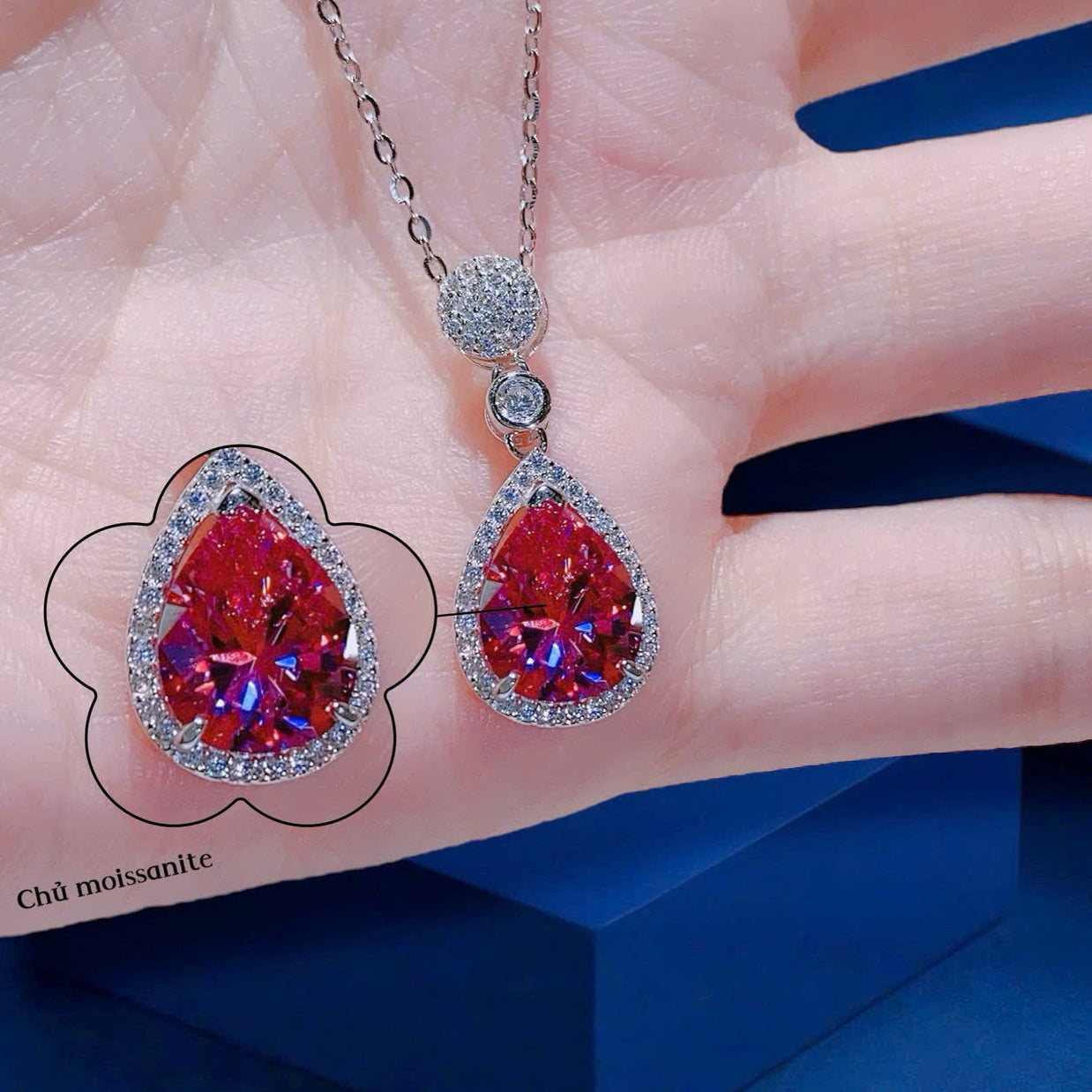 Teardrop-shaped gemstone necklace on a hand with a blue background