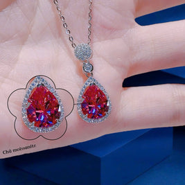 Teardrop-shaped gemstone necklace on a hand with a blue background