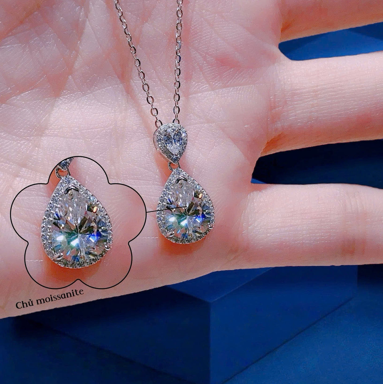 Teardrop-shaped gemstone necklace on a hand with a blue background