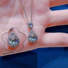 Teardrop-shaped gemstone necklace on a hand with a blue background