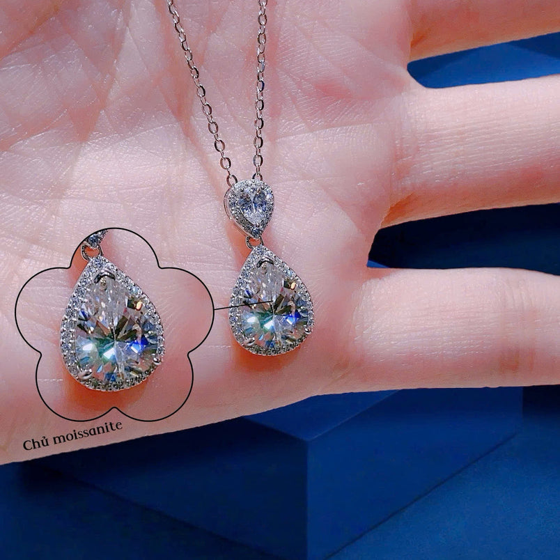 Teardrop-shaped gemstone necklace on a hand with a blue background