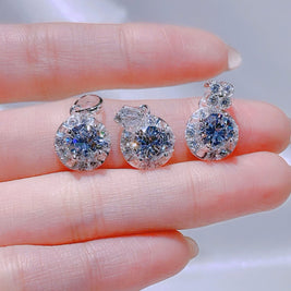 Three diamond earrings displayed on a hand with a blurred background