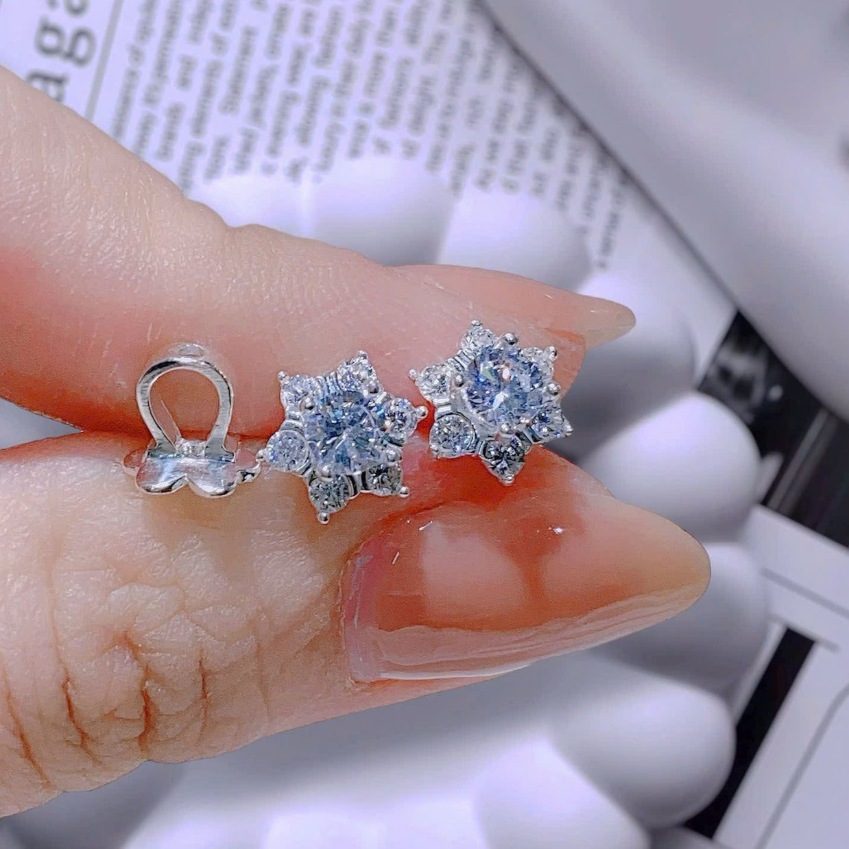 Three diamond earrings held between fingers on a newspaper background