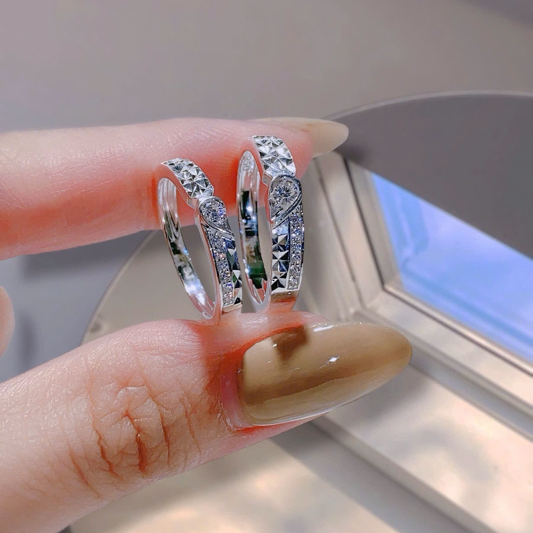 Three silver rings with gemstones on a finger against a neutral background