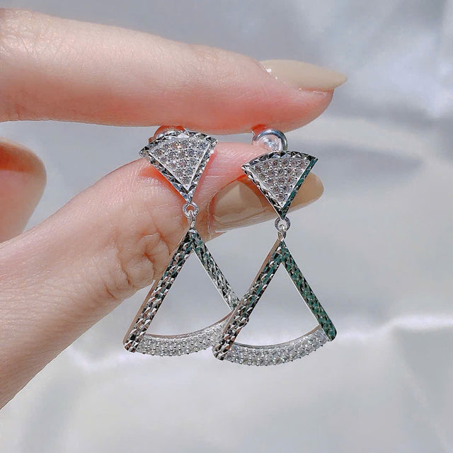 Triangle-shaped earrings held by a hand against a neutral background