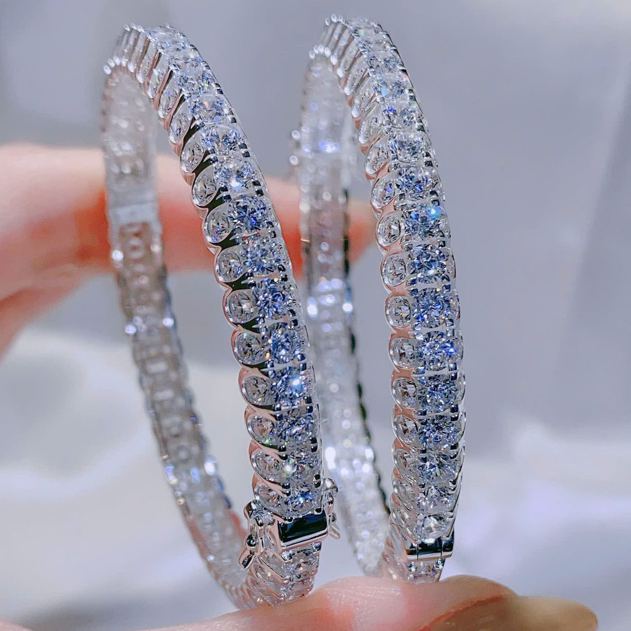 Two diamond bracelet held between fingers against a blurred background