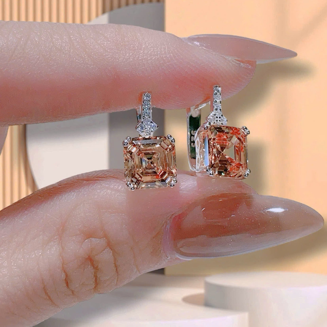 Two diamond earrings held between fingers against a neutral background