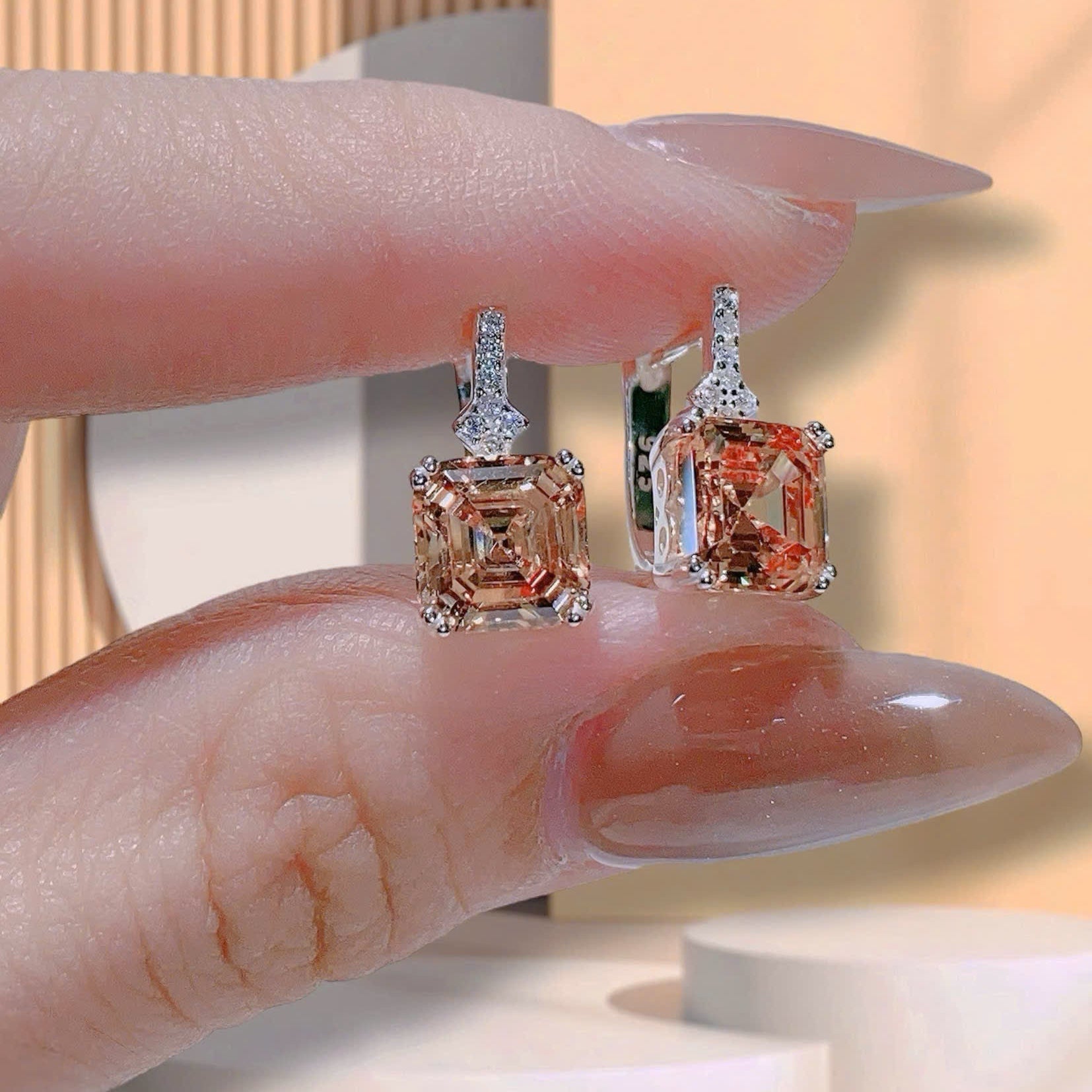 Two diamond earrings held between fingers against a neutral background