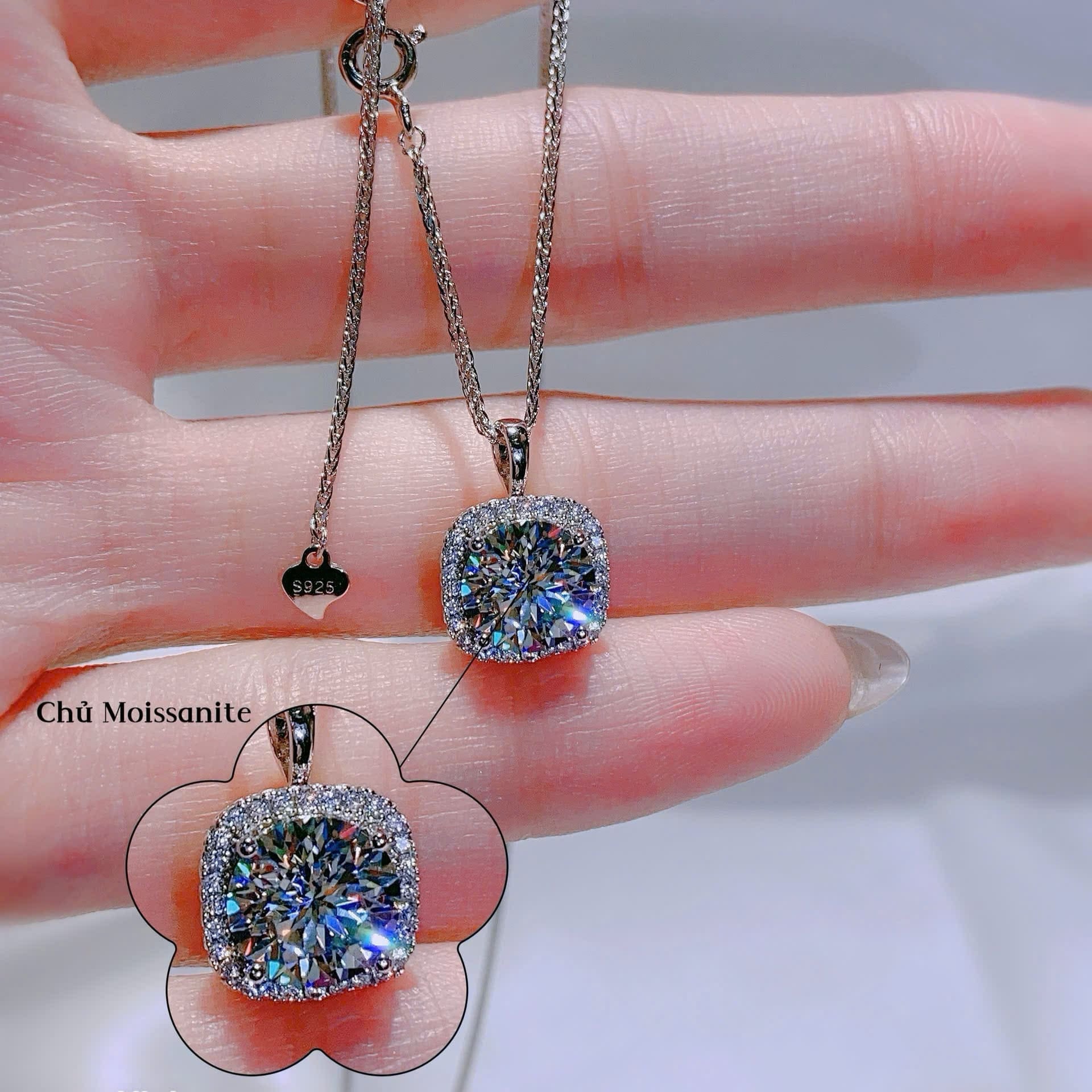 Two diamond pendants on a chain held by a hand with a blurred background