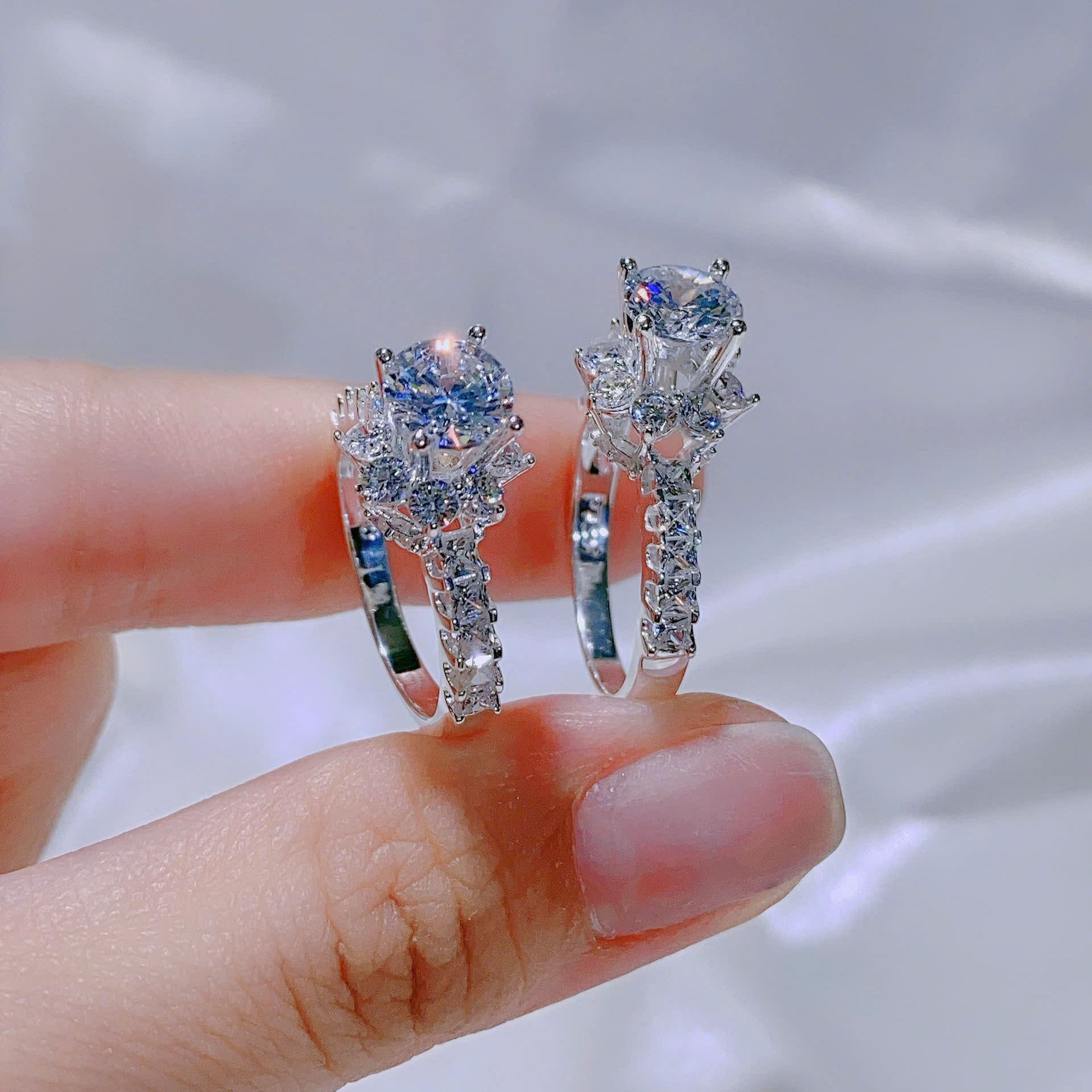 Two diamond rings held between fingers against a blurred background