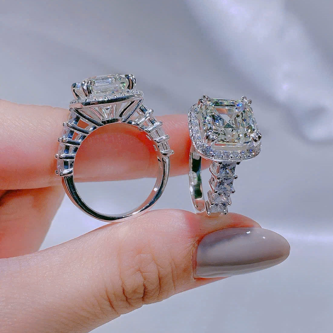 Two diamond rings held between fingers against a neutral background