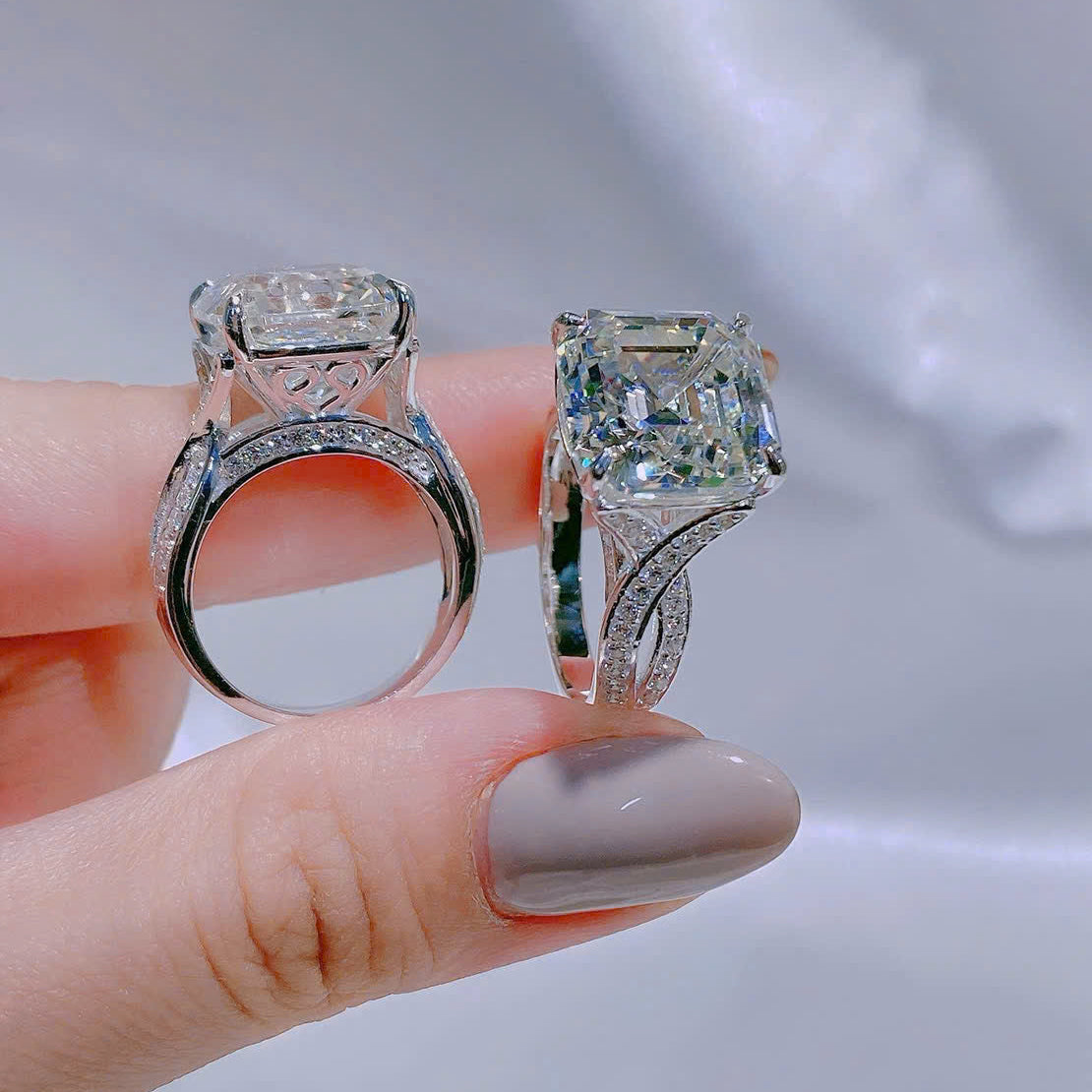 Two diamond rings held between fingers against a neutral background