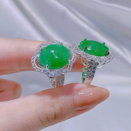 Two green gemstone rings with silver settings held on a hand against a neutral background.