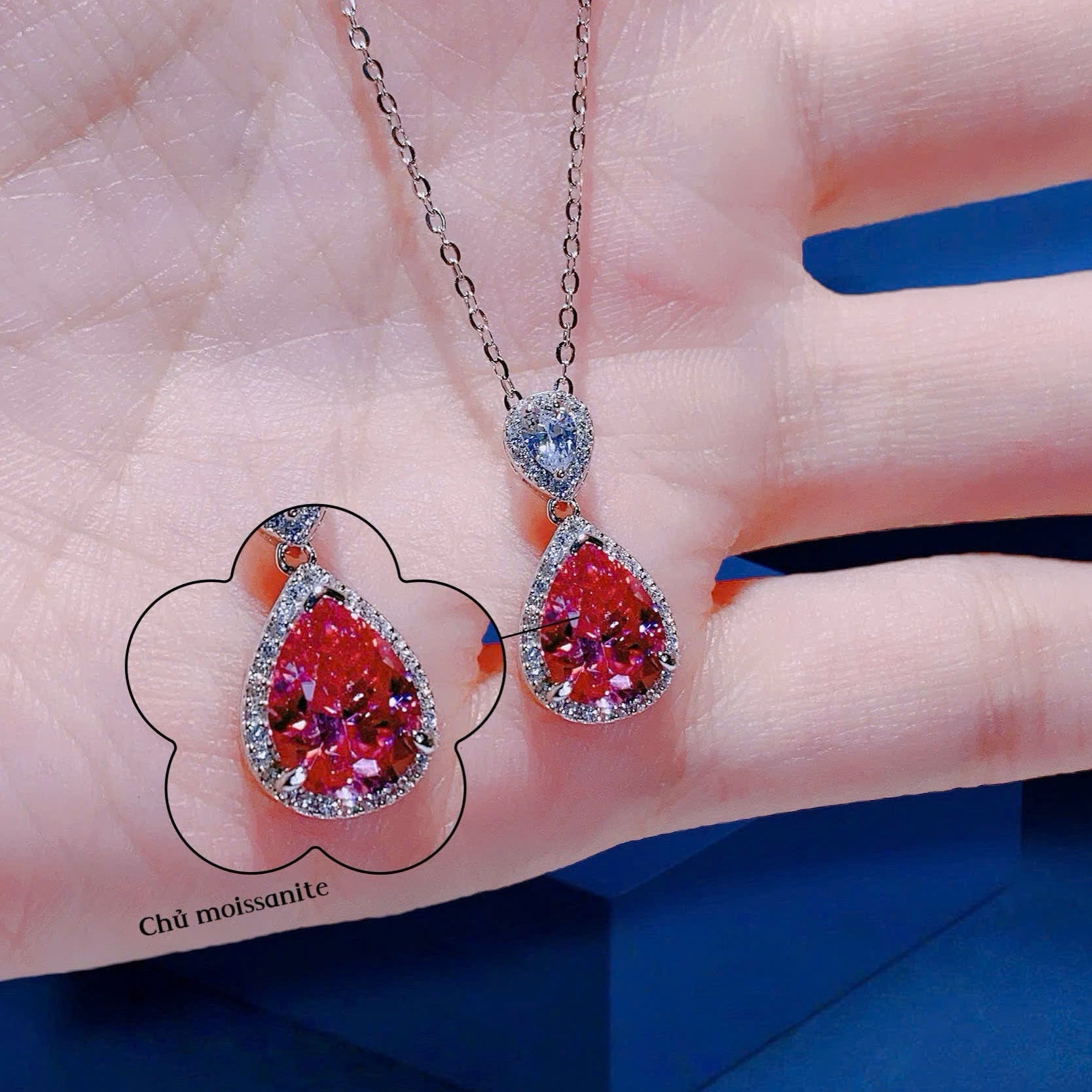 Two red gemstone pendants on a chain held in a hand with a blue background.