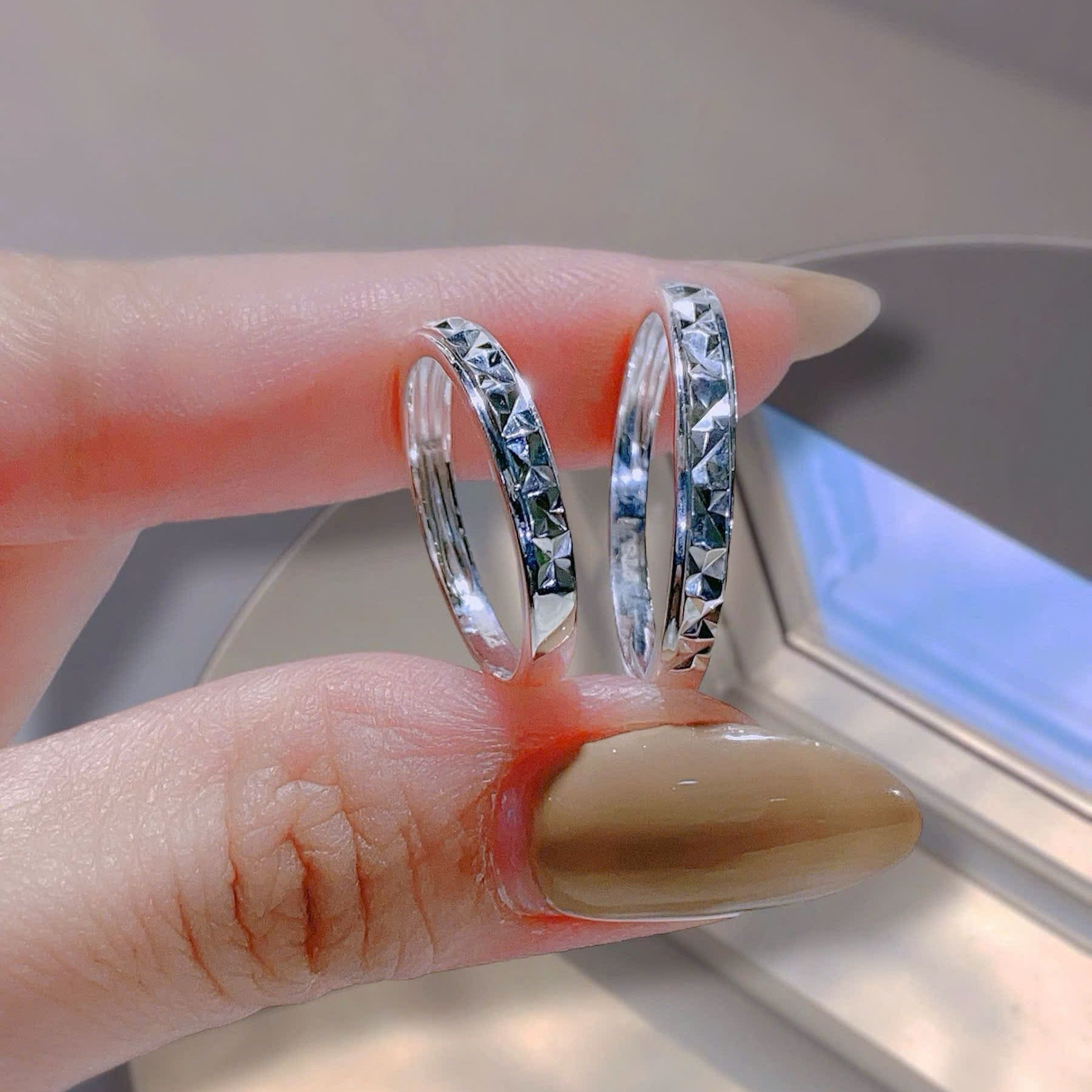 Two silver rings being worn on a finger with a neutral background