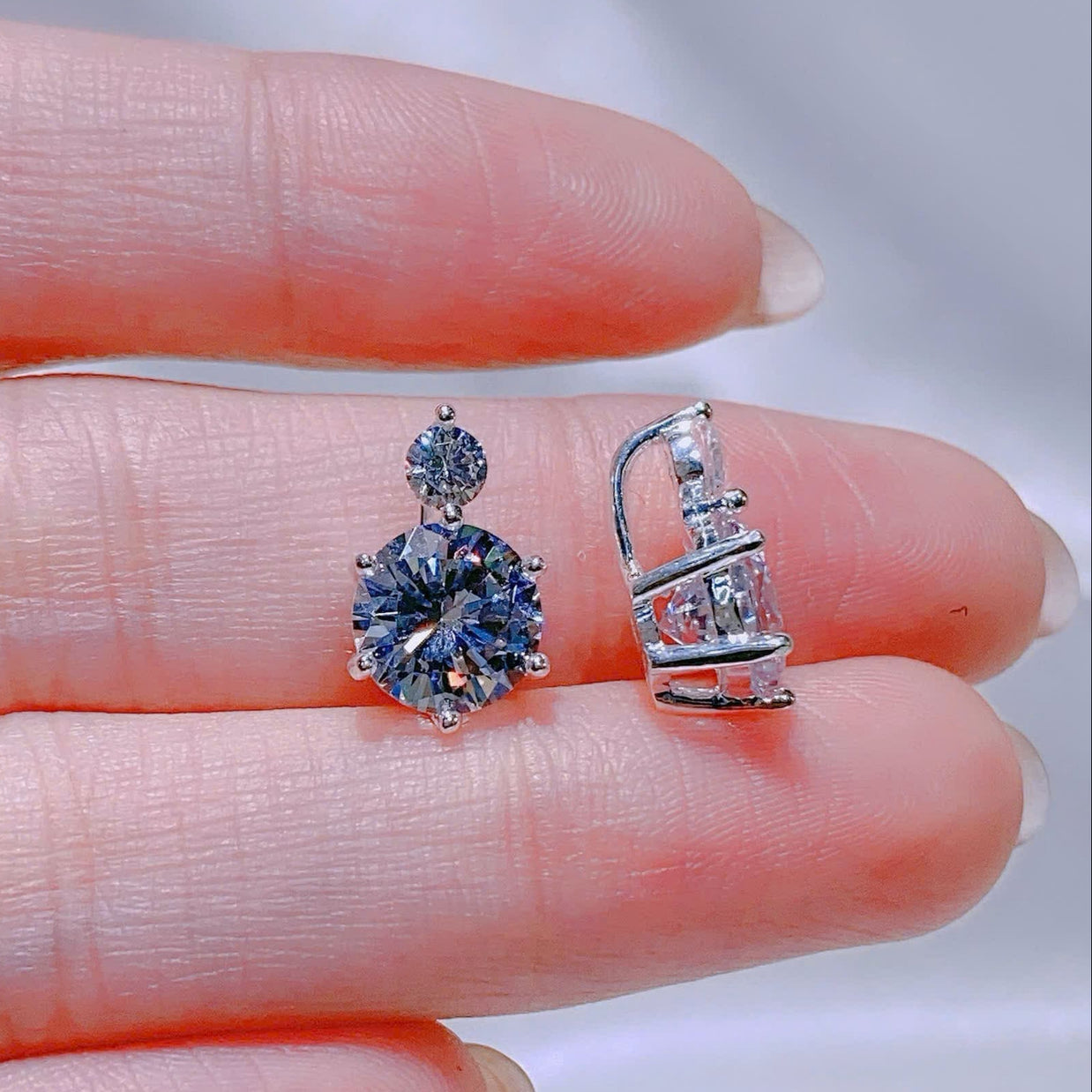 Two silver earrings held between fingers against a neutral background