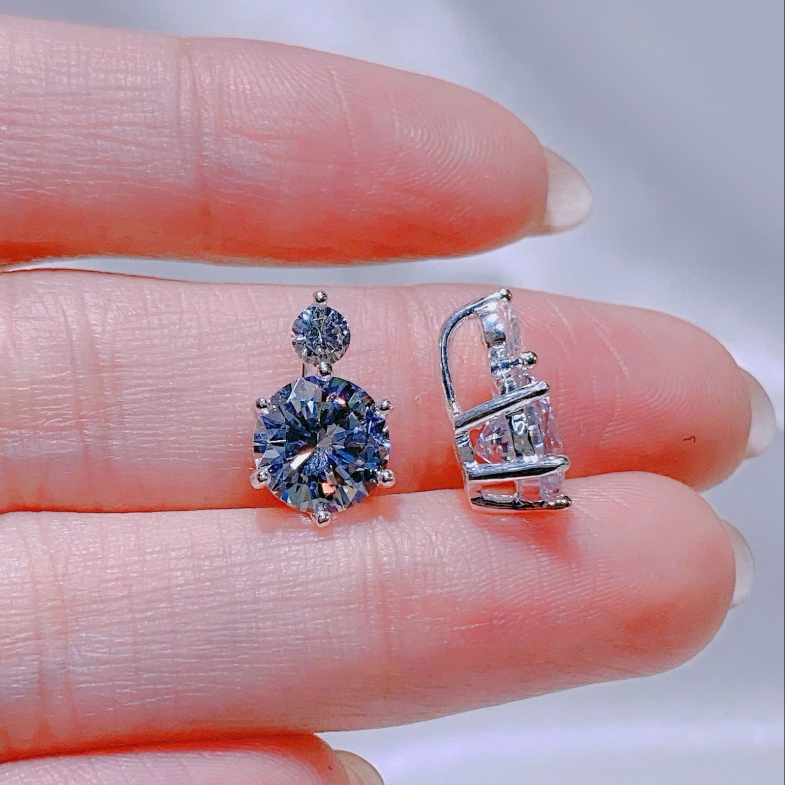 Two silver earrings held between fingers against a neutral background