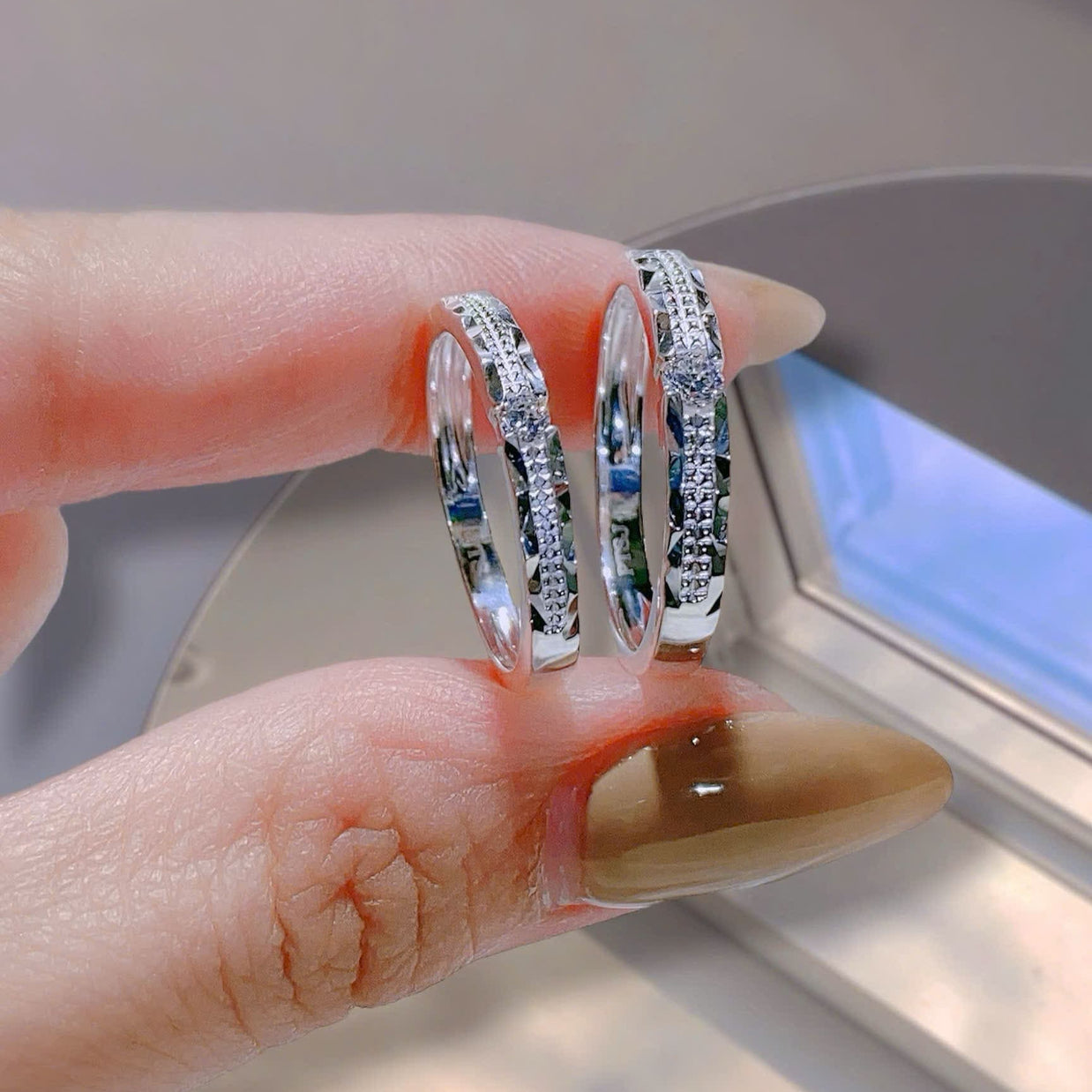 Two silver hoop earrings being held between fingers with a blurred background