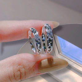 Two silver hoop earrings being held between fingers with a neutral background