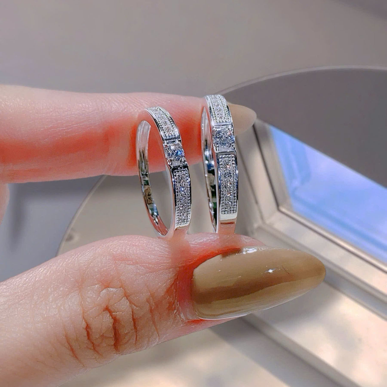 Two silver hoop earrings with embedded stones held between fingers against a neutral background.
