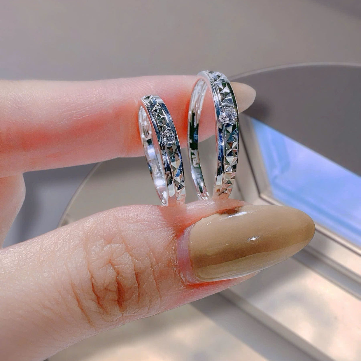 Two silver rings being worn on a finger with a neutral background
