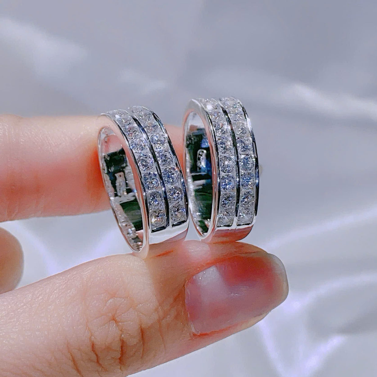 Two silver rings with gemstones held between fingers against a blurred background