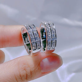 Two silver rings with gemstones held between fingers against a blurred background