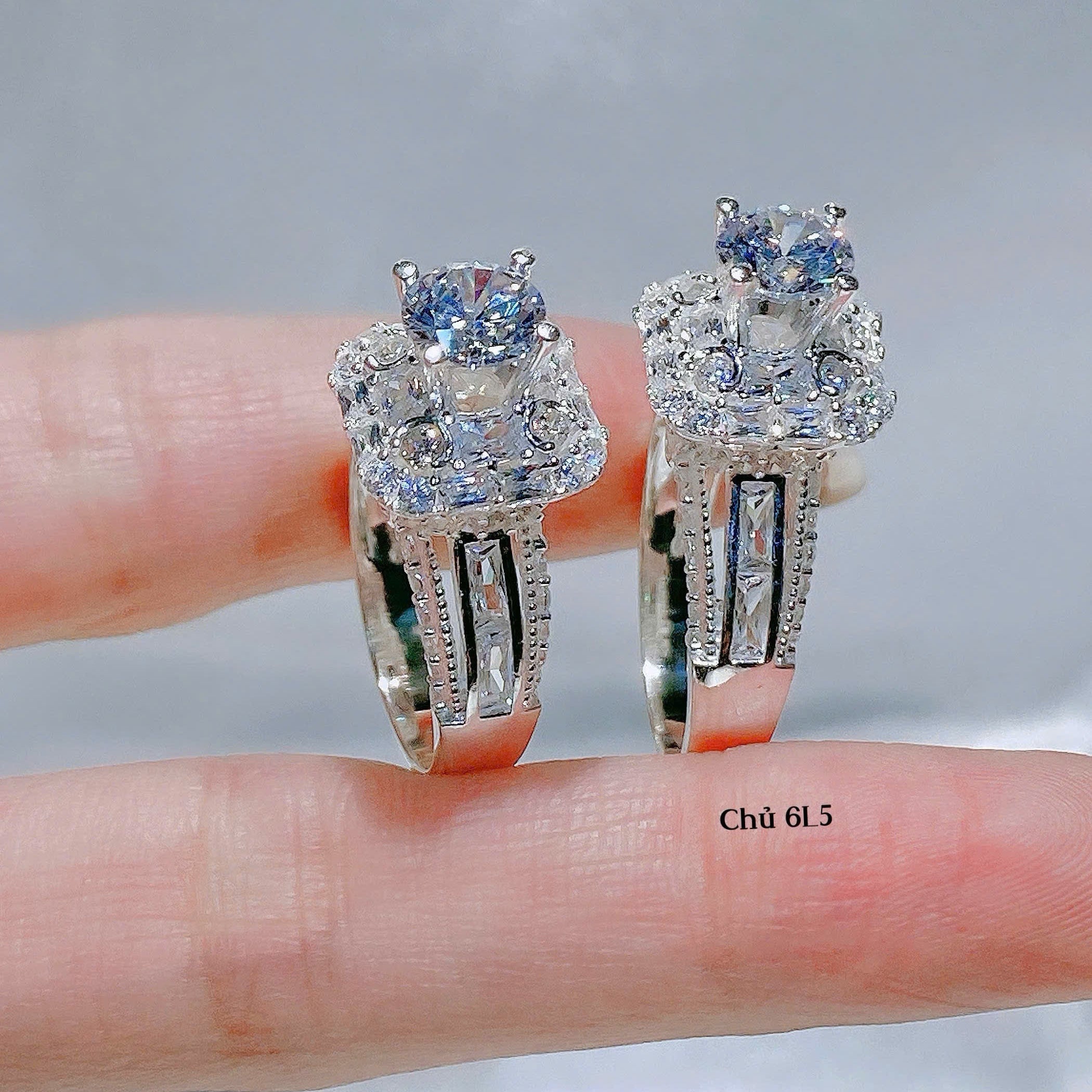 Two silver rings with gemstones on a finger against a neutral background