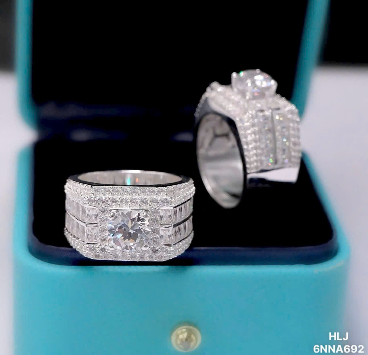 Two silver rings with gemstones on a turquoise stand.