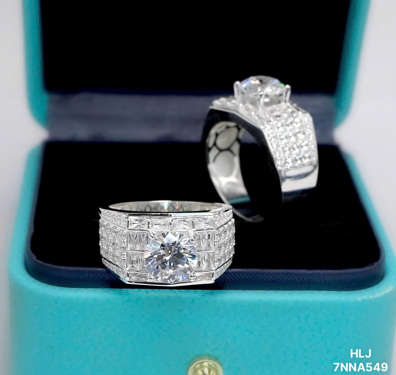 Two silver rings with large gemstones on a turquoise jewelry box.