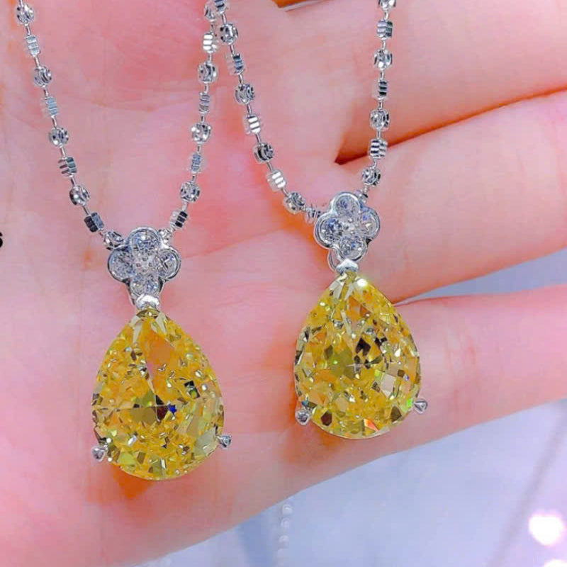 Two yellow teardrop pendants on silver chains held between fingers with a blurred background.